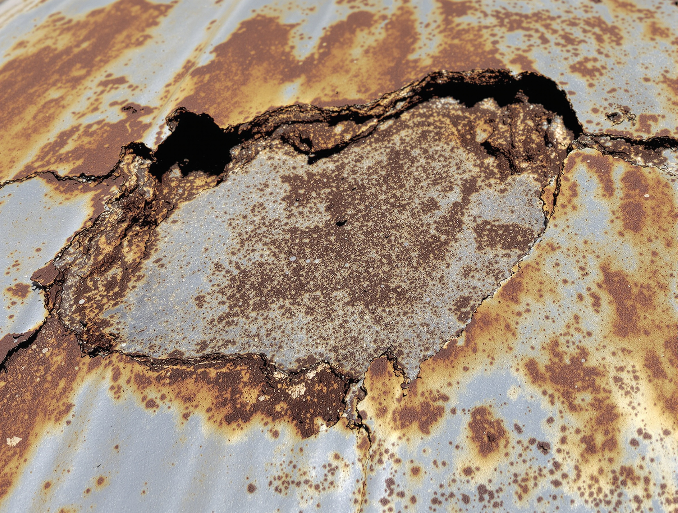 Severe corrosion failure on galvanized steel metal roof near the coast showing heavy rust, pitting, coating failure, and structural deterioration